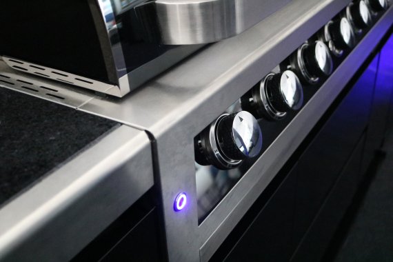 Detaljerad närbild av kontrollpanelen på en exklusiv gasolgrill, där glänsande vred i metall möter en elegant upplyst blå strömb