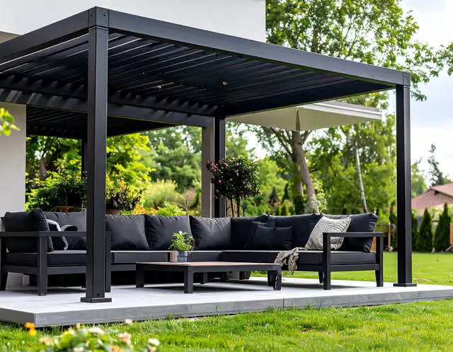 Svart lamellpergola med matchande loungesoffa och grönska i bakgrunden.