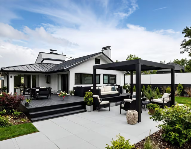 Stor uteplats med trädäck, stensatta ytor och en svart designpergola i trädgården.
